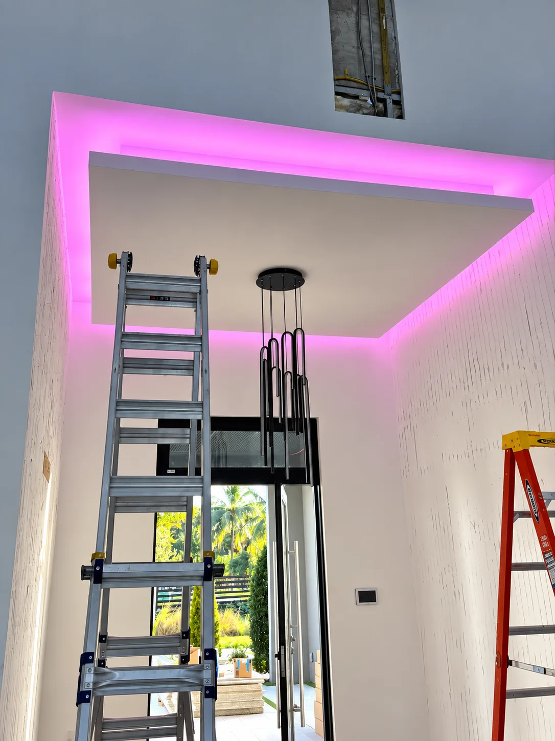 Entry chandelier hanging beneath a pink LED soffit during a luxury lighting installation in Miami-Dade